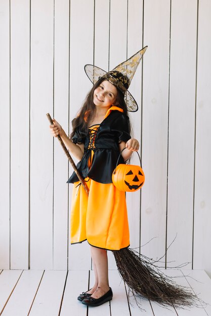 Girl in Halloween costume with pumpkin basket and broom posing in studio 