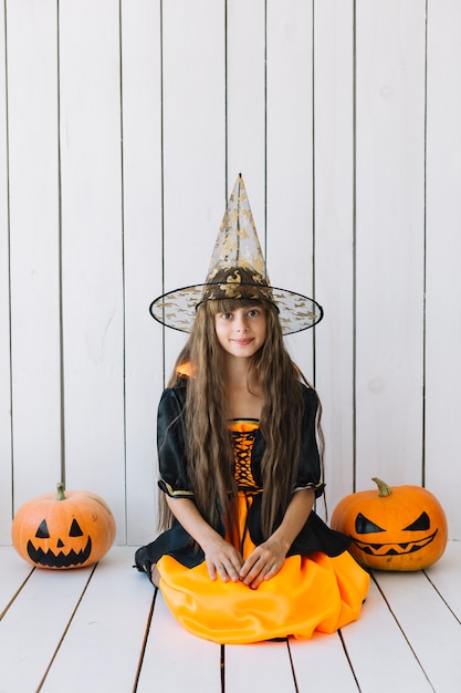 Free Photo girl in halloween costume with pumpkins on sides sitting in studio