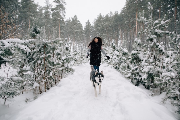 Girl have fun with her Husky dog in snowy winter pine forest