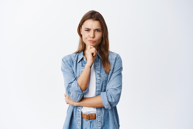 Girl having doubts Suspicious woman frowning and staring at camera thoughtful hesitating about deal standing pensive against white background