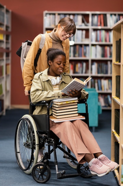 Girl helping her colleague in wheelchair choose a book for a project