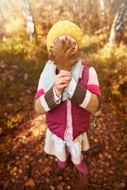 Free photo girl holding autumn leaf on her face