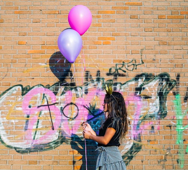 Free photo girl holding balloons in front of graffiti wall