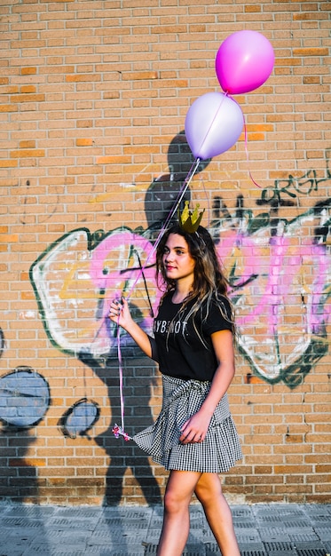 Girl holding balloons in front of graffiti wall