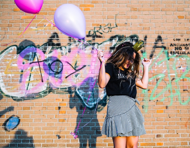 Free photo girl holding balloons in front of graffiti wall