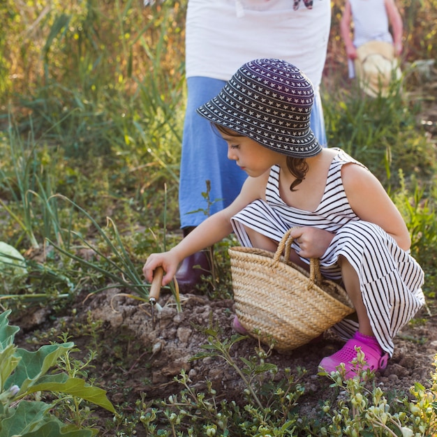 Girl holding basket digging the soil with trowel