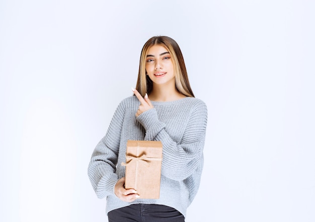 Girl holding a cardboard gift box and pointing a receiver aside.