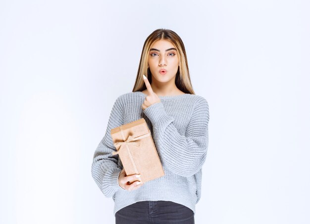 Girl holding a cardboard gift box and pointing a receiver aside.