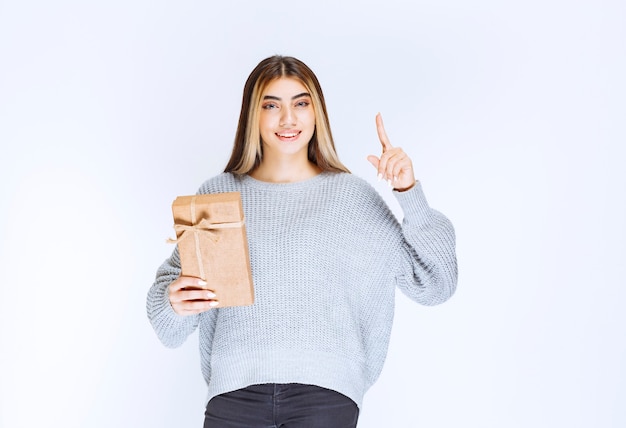 Girl holding a cardboard gift box and pointing a receiver aside.