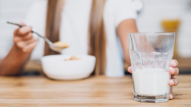 Girl holding a glass of milk while eating cereal