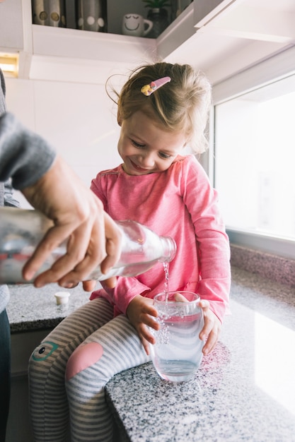 Free photo girl holding glass while her father pouring water in kitchen