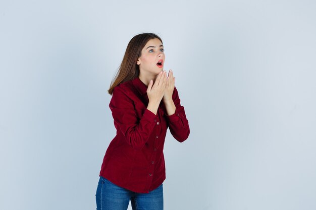 girl holding hands near open mouth while looking away in burgundy shirt and looking wondered.