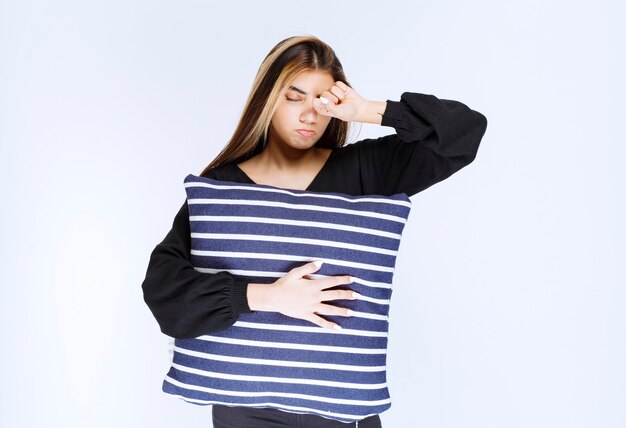 Girl holding her blue striped pillow and sleeping.