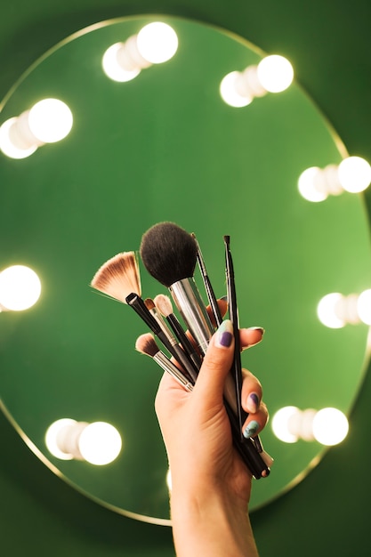 Free photo girl holding make up brushes in front of a mirror