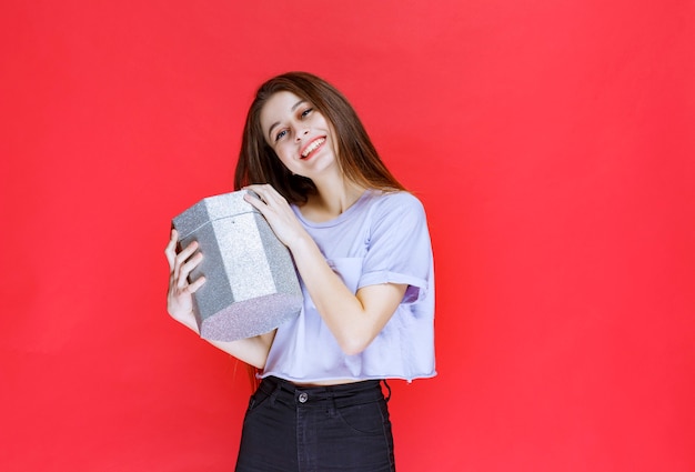 Girl holding a silver gift box and feeling happy. 