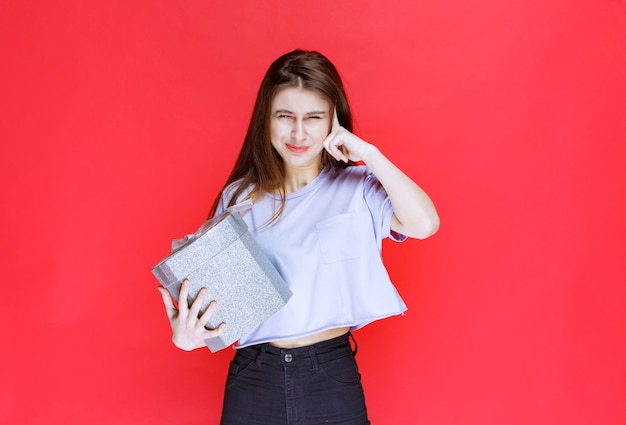 Girl holding a silver gift box and looks thoughtful. 