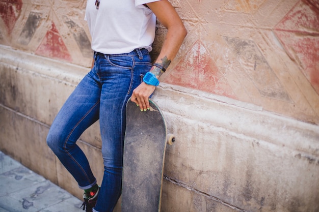 Free photo girl holding skateboard leaning on concrete wall