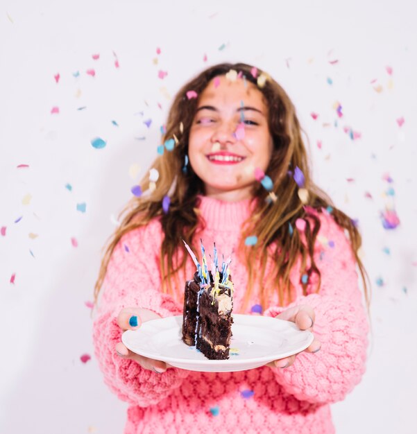 Girl holding slice of chocolate cake surrounded by confetti