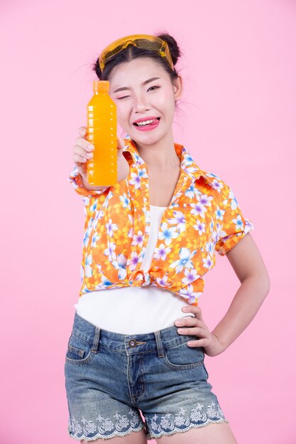 The girl holds a bottle of orange juice on a pink background.