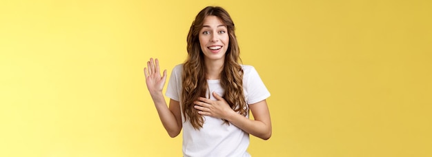 Free photo girl introduce herself friendly joyful casual conversation smiling broadly hold hand heart raise palm waving swear tell truth be honest grinning make promise oath stand yellow background say hi