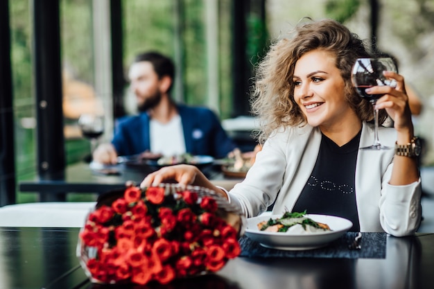 Free Photo girl is sitting at a table in the restaurant and drink wine, enjoy the scent of roses flower and waiting a date