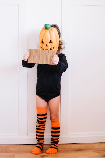 Free photo girl in jack-o-lantern mask holding cardboard