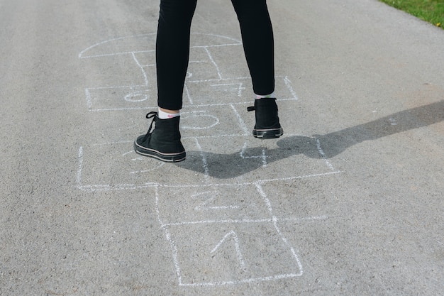 Free photo girl jumping in chalk boxes drawn on asphalt