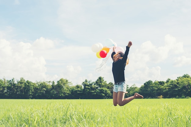 Girl jumping with balloons on the greenfield