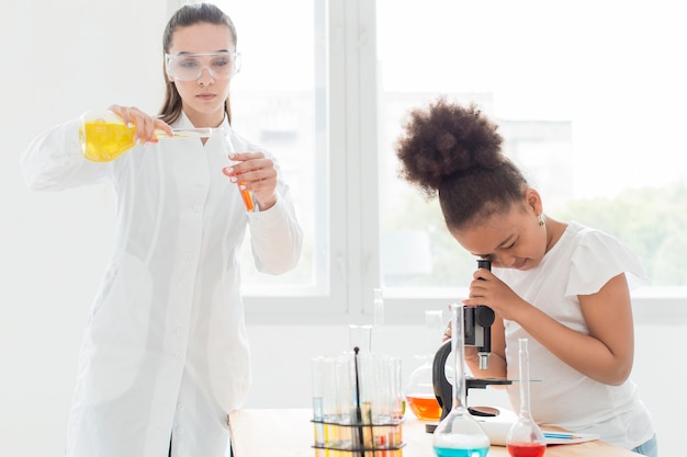 Free Photo girl looking through microscope with female scientist and potions