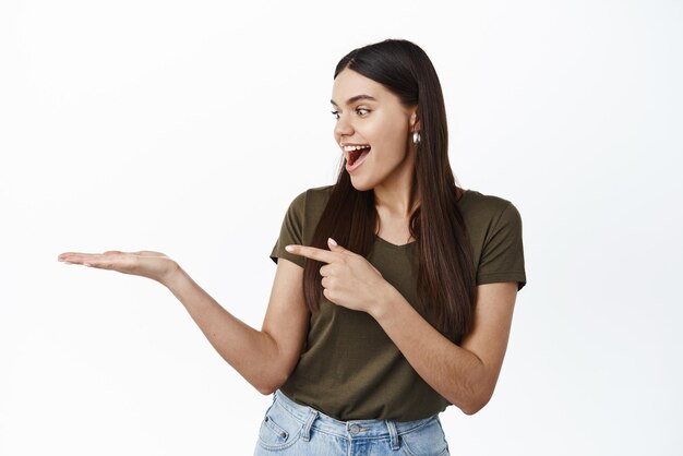 Girl looks excited at her palm with item advertisement pointing at hand against copy space standing over white background Copy space