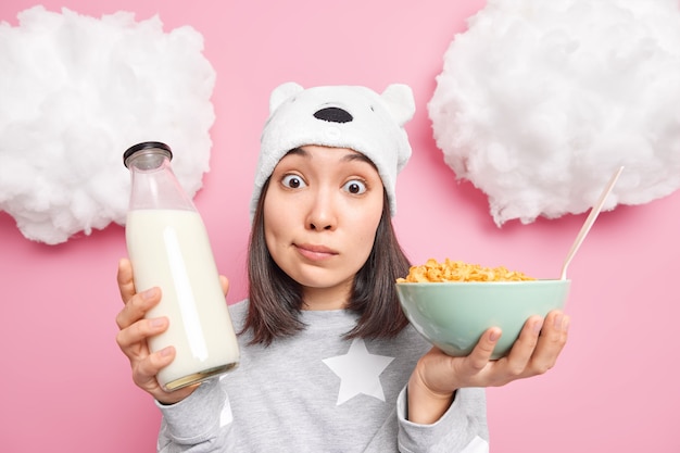 Free Photo girl looks with surprised expression at camera keeps eyes widely opened wears pajama has breakfast eats cornflakes with milk wears domestic clothes