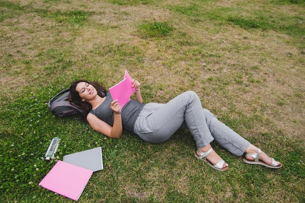 Free photo girl lying on grass reading notebook