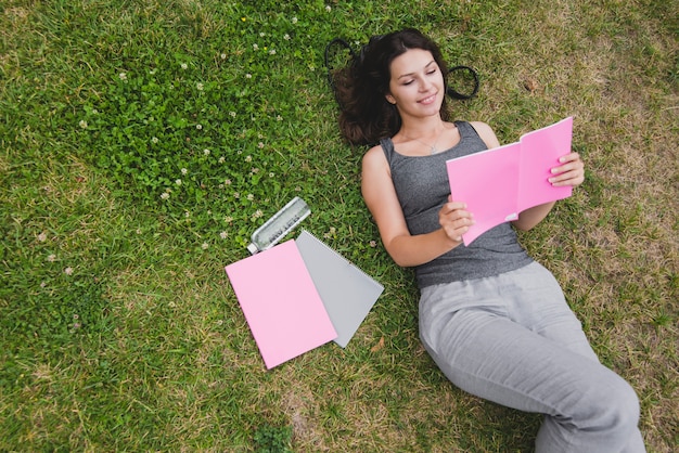 Free photo girl lying on grass reading notebook