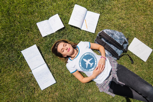 Free photo girl lying on grass surrounded by notebooks