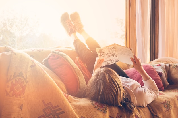 Free photo girl lying on sofa reading book