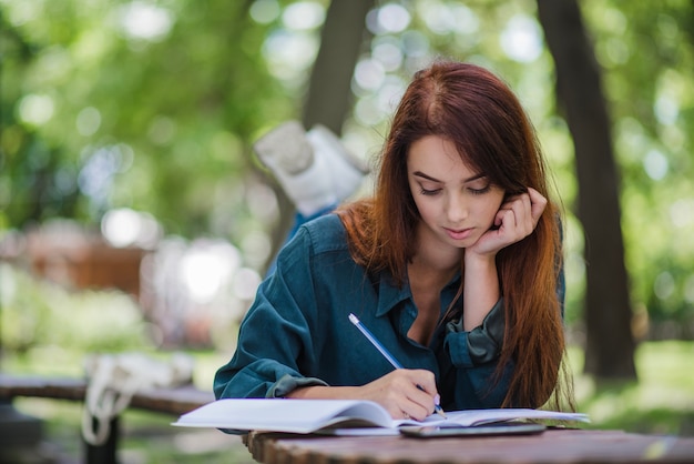 Free Photo girl lying on table in park writing