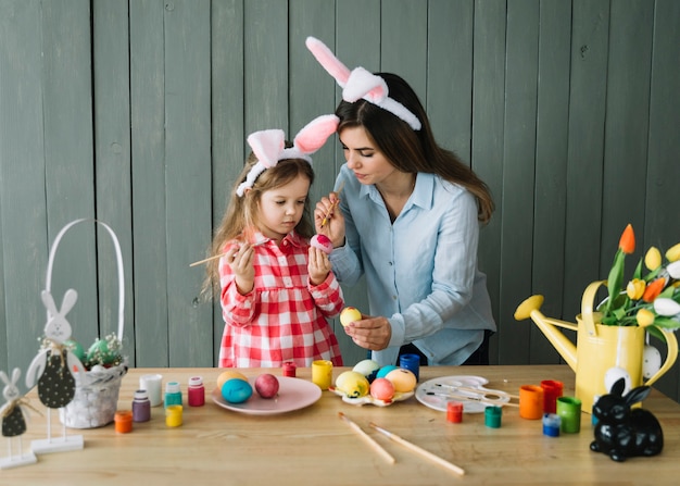 Free Photo girl and mother in bunny ears painting eggs for easter