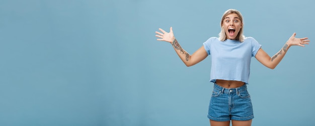 Free Photo girl overwhelmed with positive emotions and happiness being surprised rejoicing and screaming from joy spreading palms aside opening mouth from amazement standing delighted over blue wall