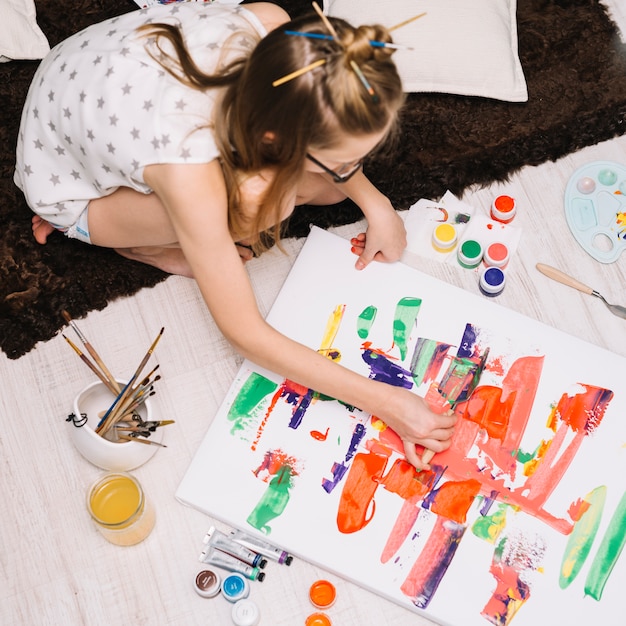 Girl painting with bright gouache on paper on floor