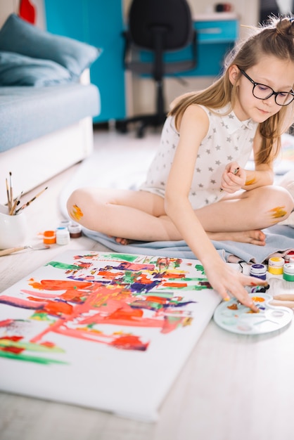 Free photo girl painting with fingers on canvas on floor