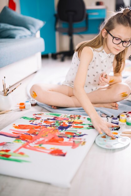 Girl painting with fingers on canvas on floor