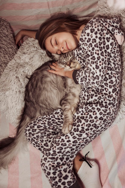 Free photo girl in pajamas hugging her cat and laying on the bed