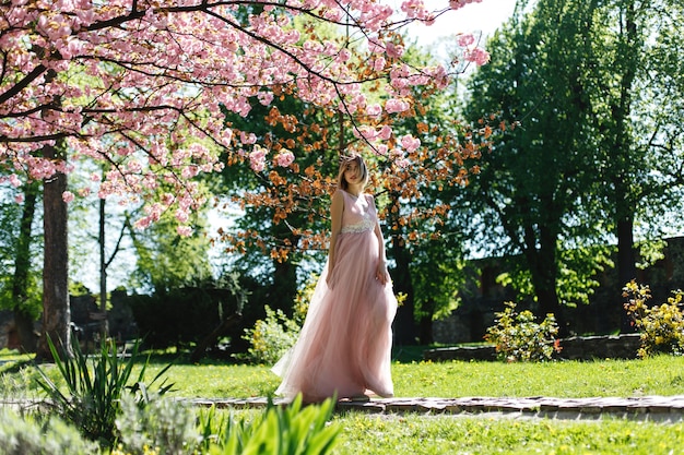 Girl in pink dress stands under blooming sakura tree in the park