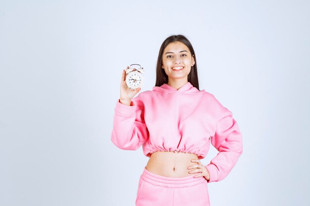 Girl in pink pajamas holding an alarm clock and promoting it as a product. 