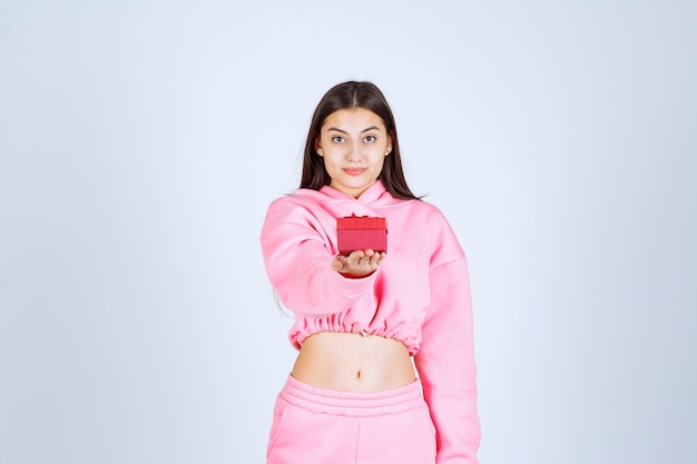 Girl in pink pajamas holding a small red gift box and offering it to her friend. 