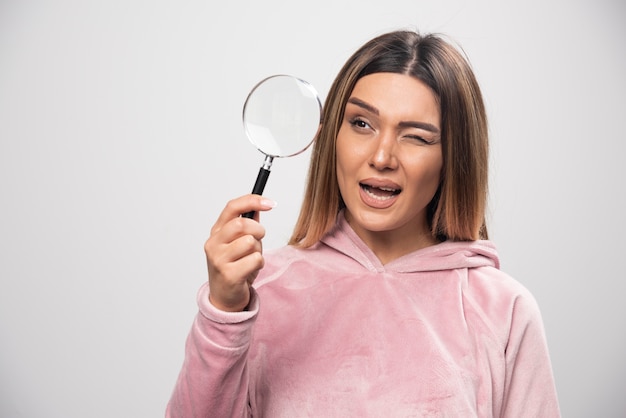 Girl in pink swaetshirt putting a magnifier to her eye and looking through it