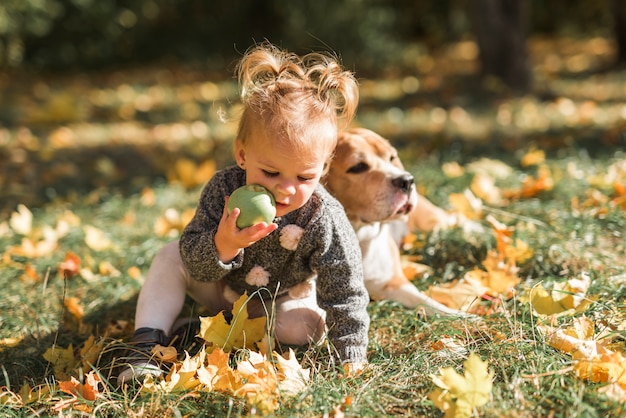 Free Photo girl playing with ball sitting in grass near her dog at park