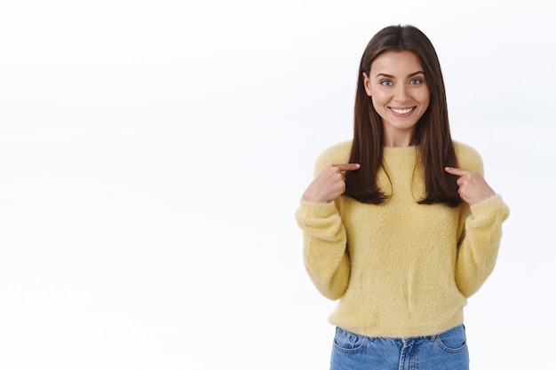 Girl pointing at herself and smiling as suggest own help, personal candidature, express willingness to participate in event, grinning and looking ready for tasks, standing white wall