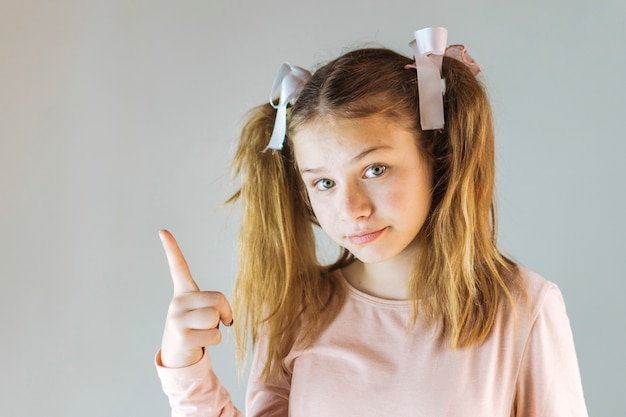 Free photo girl pointing up on grey background