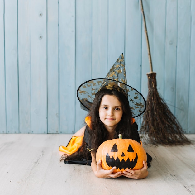 Girl in pointy hat and broom holding pumpkin